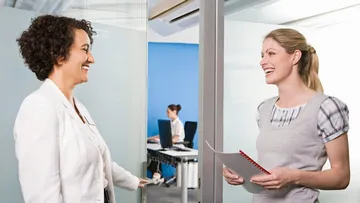 Zwei Frauen reden lachend vor einem Büro miteinander.