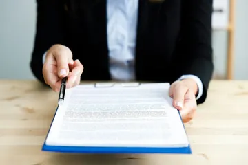 Eine Person gibt ein Dokument und einen Stift zum Unterschreiben.