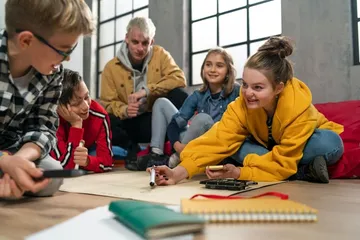 Drei Personen sammeln Müll in einem Park mit Bäumen. Ein Kind mit pinker Mütze füllt einen roten Sack. Eine Erwachsene und ein weiteres Kind helfen mit.