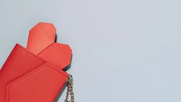 Aus einer roten Geldbörse schauen zwei Papierherzen heraus.