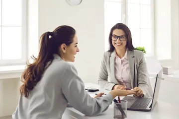 Zwei Frauen reden lächelnd am Schreibtisch miteinander.