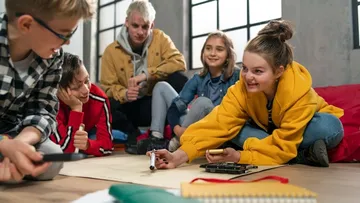 Drei Personen sammeln Müll in einem Park mit Bäumen. Ein Kind mit pinker Mütze füllt einen roten Sack. Eine Erwachsene und ein weiteres Kind helfen mit.
